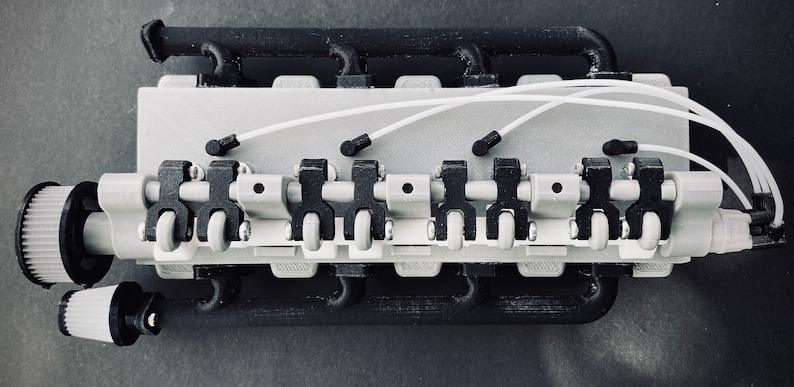May include: A close-up of a 3D printed model of a small engine with white wires and black and grey components.