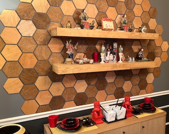 May include: A dining room with a decorative wall of wooden hexagon tiles. Two wooden shelves display figurines and decorative items. A wooden cabinet holds red dishes and Chinese takeout containers. A large bamboo plant sits in a dark pot.