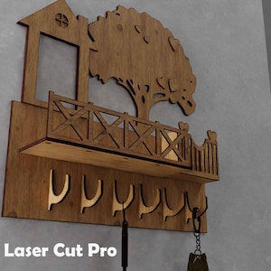 May include: Wooden key holder with a house and tree design. Features a shelf, decorative railing, and key hooks. The key holder is made of brown wood and is mounted on a grey wall. The text "Laser Cut Pro" is visible in the lower left corner.