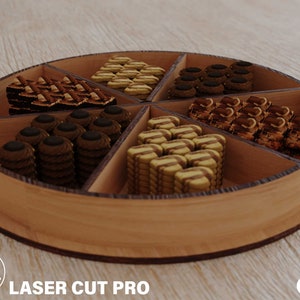 May include: A wooden serving tray with six compartments, each filled with different types of cookies and pastries. The tray is round with a light brown finish. The text "LASER CUT PRO" is visible on the bottom left.