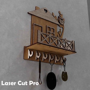 May include: Wooden key holder shaped like a house with an owl perched on the roof. The house has a small balcony with a railing and a shelf below. There are six hooks on the shelf for hanging keys.