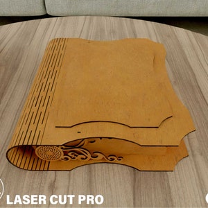 May include: A wooden book-shaped box with intricate laser-cut designs. The box is closed and has a brown finish.