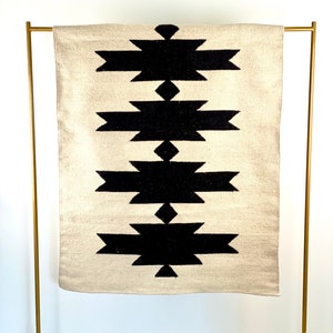 May include: A white and black geometric rug with a diamond pattern. The rug is hanging on a gold metal stand.