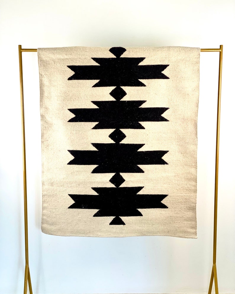 May include: A white and black geometric rug with a diamond pattern. The rug is hanging on a gold metal stand.