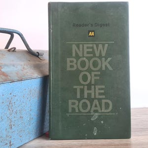 May include: A vintage green "New Book of the Road" by Reader's Digest, with the AA logo. The book is standing upright next to a weathered blue toolbox with a metal handle. The book's title is in large, bold letters.