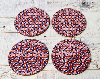 May include: Four round coasters with a repeating pattern of the Union Jack flag in red, white, and blue. The coasters are arranged in a square formation on a light-colored wooden surface. The coasters are a decorative item.