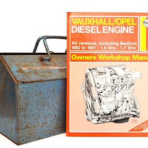 Könnte beinhalten: Ein Haynes Owners Workshop Manual für Vauxhall/Opel Dieselmotoren, das alle Versionen einschließlich Bedford von 1982 bis 1991 mit einem 1,6-Liter- und einem 1,7-Liter-Motor abdeckt. Das Handbuch befindet sich neben einer blauen Metallwerkzeugbox mit Rost.