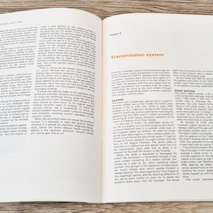 May include: A close-up of two pages from a vintage car repair manual. The pages are open to Chapter 8, Transmission System. The text discusses the clutch and clutch servicing. The pages are printed on white paper with black text.