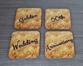 May include: Four square coasters with a rustic, aged paper texture. The coasters feature the words "Golden", "50th", "Wedding", and "Anniversary" in black script.