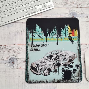Può includere: Un'illustrazione in bianco e nero di un'auto Volvo 240 serie su uno sfondo blu e verde con schizzi di vernice nera. Il testo "VOLVO 240 SERIES" è stampato sull'immagine.