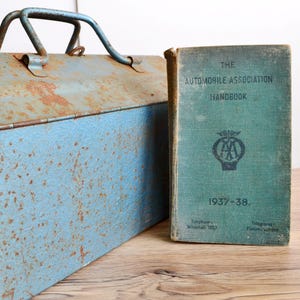May include: A vintage blue metal toolbox with rust and a green book titled "The Automobile Association Handbook 1937-38."