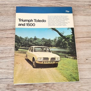 May include: A vintage book cover for a Triumph Toledo and 1500 car maintenance manual. The cover features a yellow car with a license plate that reads "KXC 767M" and a green background with a lake and trees.