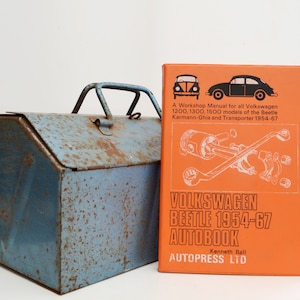 May include: An orange and white Volkswagen Beetle 1954-67 Autobook workshop manual with a blue metal toolbox. The book cover features a diagram of a car engine and the text "A Workshop Manual for all Volkswagen 1200, 1300, 1500 models of the Beetle. Karmann-Ghia and Transporter 1954-67" and "VOLKSWAGEN BEETLE 1954-67 AUTOBOOK Kenneth Ball AUTOPRESS LTD".
