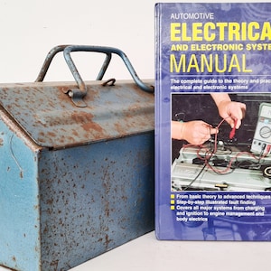 May include: A blue metal toolbox with rust and a Haynes Automotive Electrical and Electronic Systems Manual book. The book cover features a photo of a person working on a car engine.