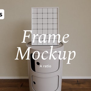 Könnte beinhalten: Ein weißer Bilderrahmen mit einem Gittermuster steht auf einem kleinen, runden, zweistöckigen Aufbewahrungselement in hellgrau. Das Element hat einen schwarzen Punkt auf der Vorderseite der oberen Ebene. Der Text "Frame Mockup" ist in Weiß unter dem Rahmen geschrieben, und "A ratio" ist in Weiß unter dem Text geschrieben. Das Aufbewahrungselement steht auf einem Holzboden.