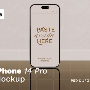 May include: A mockup of a black iPhone 14 Pro with a white screen displaying the text "PASTE design HERE". The phone is on a light gray background with a gold reflective surface below it.