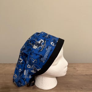 Può includere: Un cappello blu con un motivo con la scritta "Ravenclaw" e illustrazioni di corvi. Il cappello ha un bordo nero ed è esposto su una testa di manichino bianca. Questo è probabilmente un accessorio a tema.