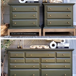 May include: Olive green dressers with gold-toned hardware. The dressers have multiple drawers and are set on a light wood base. Decorative items, including vases and books, are displayed on top. The text "PARIS LONDON NEW YORK" is visible.