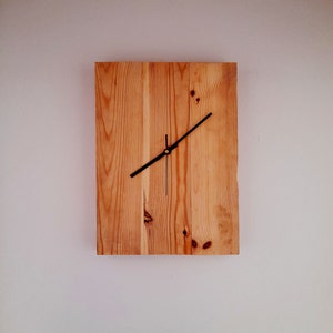 Może przedstawiać: Drewniany zegar z czarnymi wskazówkami i złotym środkiem. Zegar wykonany jest z odzyskanych drewnianych desek.