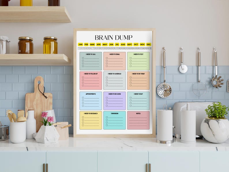 May include: A framed "Brain Dump" planner with colorful boxes for notes. The planner includes sections for calls, emails, and appointments. The background shows a kitchen setting with jars, a cutting board, and a plant.