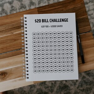 Może przedstawiać: Biały notes ze spiralnym czarnym oprawieniem. Na okładce widnieje tekst "$20 BILL CHALLENGE" i "$20*100 = $2000 SAVED". Notes jest wypełniony 100 k&oacute;łkami, z kt&oacute;rych każde zawiera tekst "$20".