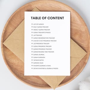 May include: A white sheet of paper with a black heading "TABLE OF CONTENT" and a list of items related to Quran study, including "List of Surahs", "Daily Quran Tracker", "Weekly Quran Tracker", "Surah Tracker (5 pages)", "Juz Tracker", "Surah Memorization Tracker", "Ayah by Ayah Progress Tracker", "Juz Progress Tracker", "Surah Progress Tracker", "Quran Progress Tracker", "Quran Reading Time Tracker", "Quran Journal", "Surah Overview", "Tafseer Notes", "Quranic Duas", "Favorite Quranic Ayahs", and "30 Days Khatam-ul-Quran (2 pages)".