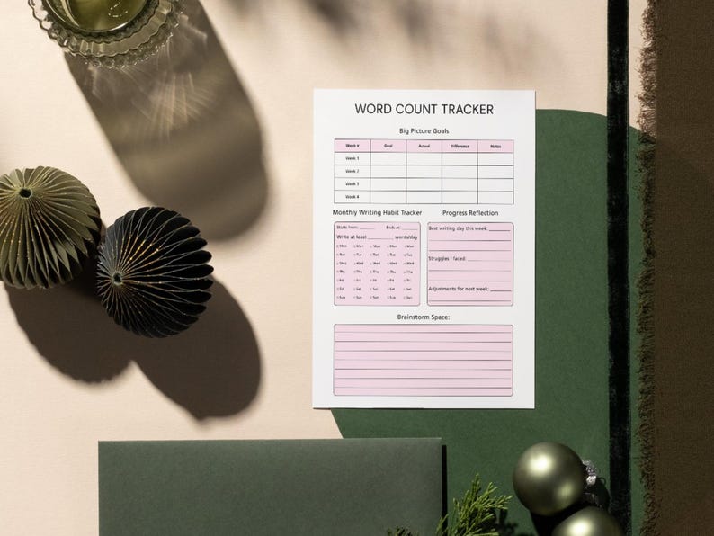 May include: A Word Count Tracker sheet with pink accents lies on a light beige surface. The sheet includes sections for weekly goals, a monthly writing habit tracker, and a space for brainstorming. Decorative paper ornaments and a glass are also visible.