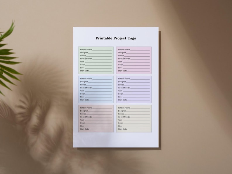May include: A white sheet of paper with the text "Printable Project Tags" at the top. The paper has six project tag templates, each with fields for pattern name, designer, source, hook/needle, yarn, color, size, and start date.