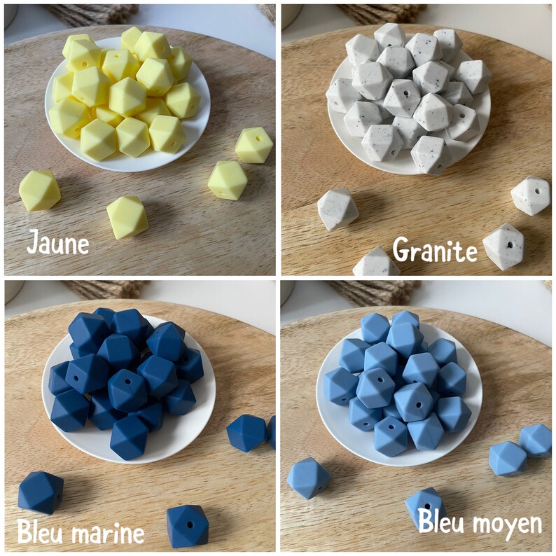 May include: Four sets of silicone teething beads in different colors: yellow, gray, dark blue, and light blue. Each set is arranged in a small white bowl on a wooden surface. The colors are labeled in French: Jaune, Granite, Bleu marine, and Bleu moyen.