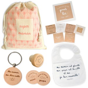 May include: A gift bag filled with a variety of items for a new mom. The bag is made of natural canvas and features a pink and white geometric pattern. The bag includes a wooden keychain with the text "Ma maman, ma M&egrave;re-veille", a wooden bottle stopper with the text "Pour arroser ce petit avec moderation", two wooden coasters with the text "C'est au tour de mam" and "C'est au tour de papa", a white bib with the text "ma maman est g&eacute;niale mon papa est terrible et moi... je leur ressemble!" and a card with the text "Un petit mot rien que pour toi".