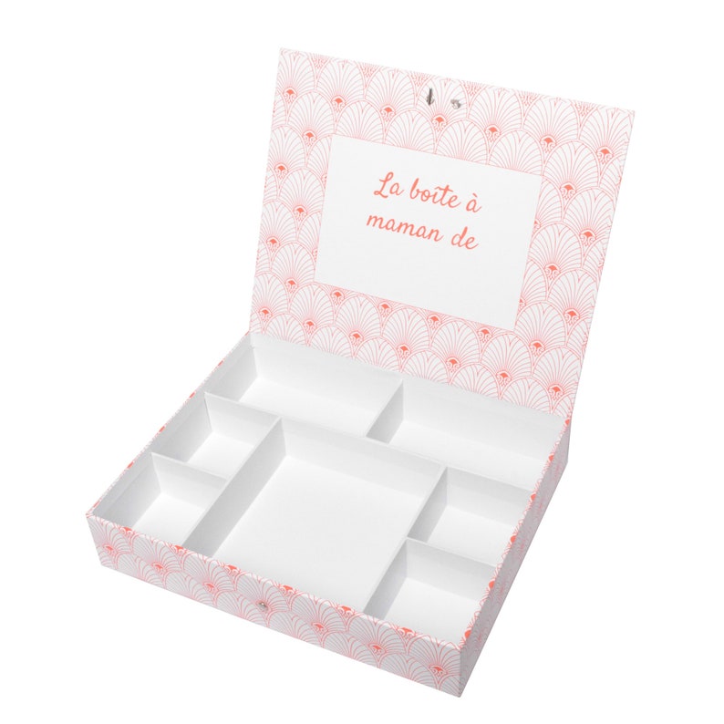 May include: White storage box with a pink and white geometric pattern on the lid and bottom. The lid is open and the box has multiple compartments inside. The lid has a label that says "La boite &agrave; maman de".
