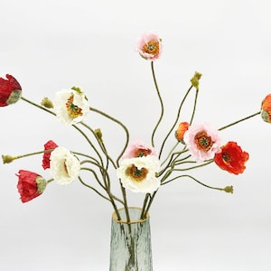 Könnte beinhalten: Ein Strauß künstlicher Mohnblumen in verschiedenen Farben, darunter Rot, Weiß, Rosa und Orange. Die Blumen sind in einer durchsichtigen Glasvase mit goldfarbenem Rand angeordnet.