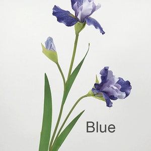 May include: A single stem of artificial blue iris flowers with two blooms and one bud. The flowers have a light purple and white center. The stem has long green leaves.