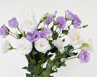 May include: A bouquet of purple and white lisianthus flowers. The flowers are arranged in a vase and have green stems and leaves.
