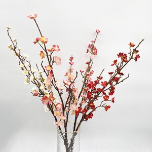 以下が含まれることがあります： 透明なガラスの花瓶に、人工の桜の枝のブーケ。枝にはピンク、白、赤の花が咲いています。