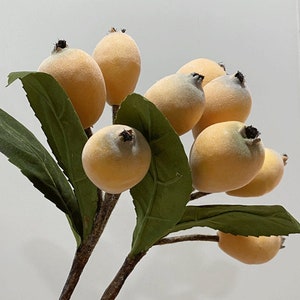 May include: A bunch of artificial yellow fruit with green leaves. The fruit is arranged in a cluster and looks like a bunch of loquats.