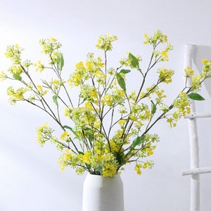 May include: A bouquet of yellow artificial flowers with green stems in a white vase.