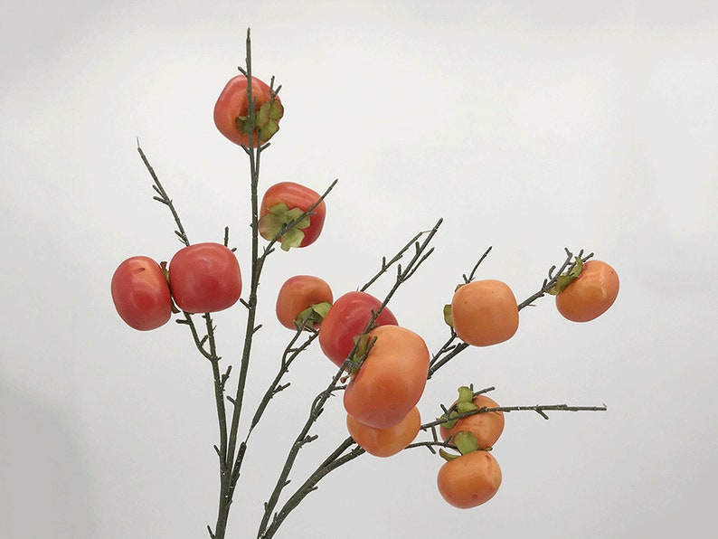 May include: A branch with multiple artificial orange and red persimmons. The persimmons are clustered together on the branch.