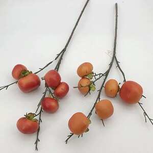 May include: Two sprigs of artificial branches with small orange and red berries. The branches are brown and have small green leaves.