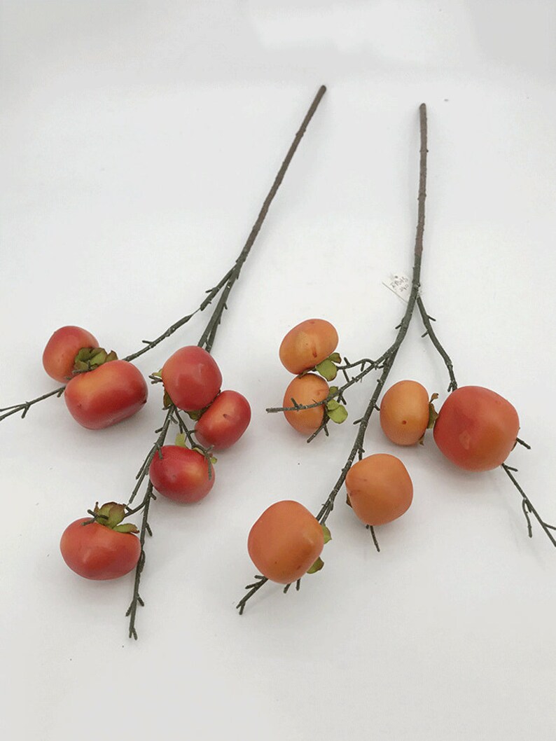 May include: Two sprigs of artificial branches with small orange and red berries. The branches are brown and have small green leaves.