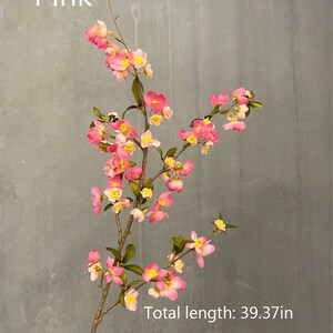 May include: A pink artificial flower branch with small pink flowers and yellow centers. The branch is 39.37 inches long.  The branch is against a gray background.