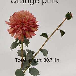 May include: A single stem artificial flower with a large orange-pink dahlia bloom and a smaller bud. The stem is green with leaves and measures 30.71 inches in length.  "Orange pink" is written above the flower.