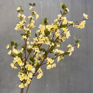 May include: A bouquet of artificial yellow flowers with green leaves on brown stems. The flowers are clustered together in a delicate arrangement.