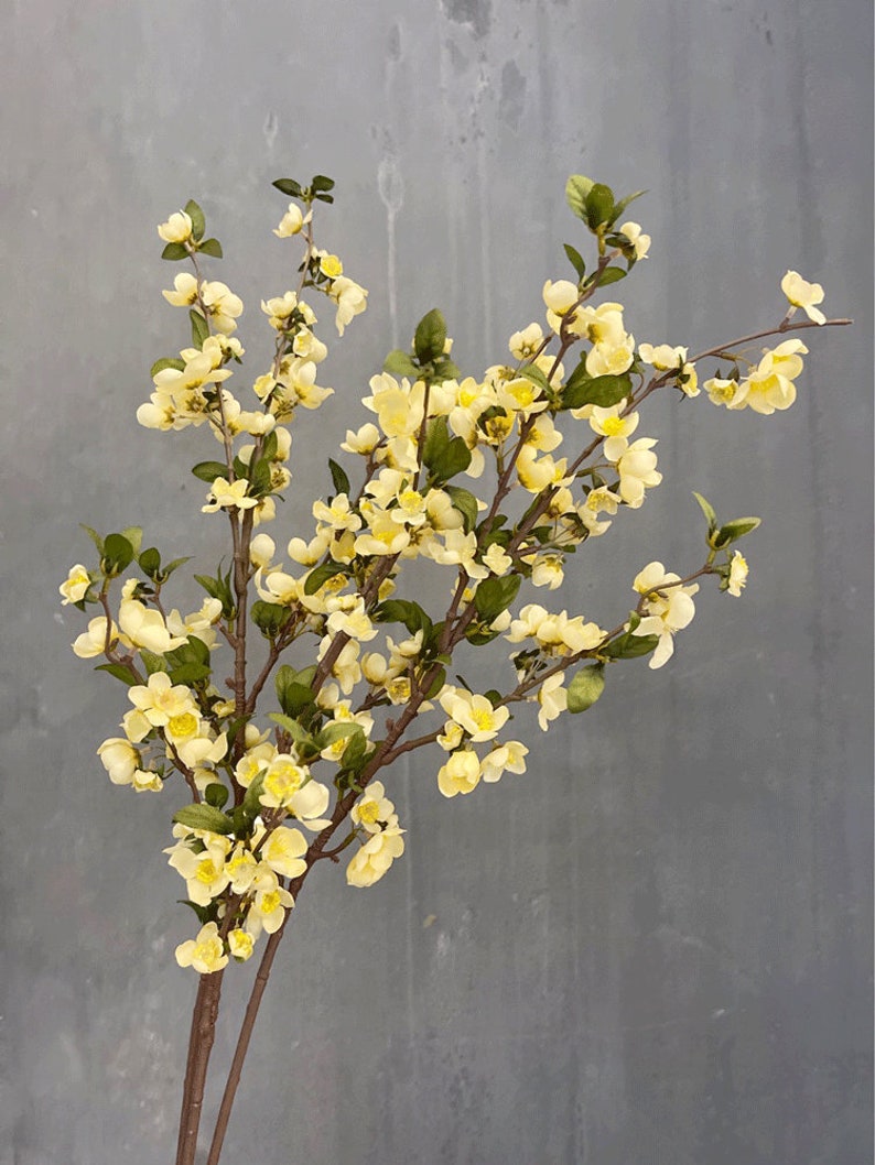 May include: A bouquet of artificial yellow flowers with green leaves on brown stems. The flowers are clustered together in a delicate arrangement.
