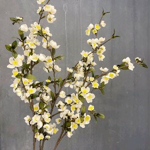 May include: A bouquet of artificial white flowers with yellow centers. The flowers are arranged on three stems and have green leaves.