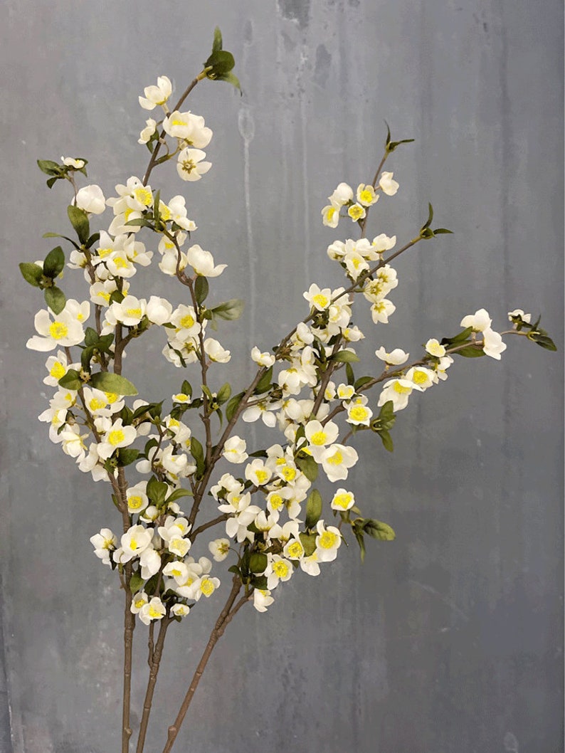 May include: A bouquet of artificial white flowers with yellow centers. The flowers are arranged on three stems and have green leaves.