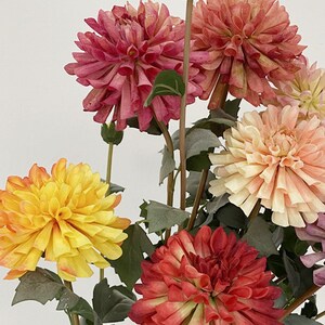 May include: A bouquet of artificial flowers with pink, yellow, and red dahlias. The flowers are arranged in a vase and have green stems and leaves.