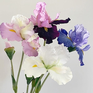 Peut inclure: Un bouquet de fleurs d'iris artificielles dans des tons de violet, rose et blanc. Les fleurs ont des pétales délicats et sont disposées en grappe.