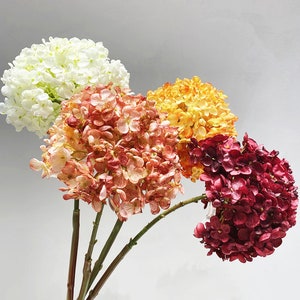 May include: A bouquet of four artificial hydrangea flowers in different colors. The flowers are white, pink, orange, and burgundy.