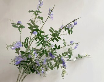 May include: A bunch of artificial purple and white flowers with green leaves. The flowers are arranged in a bouquet and have a delicate, romantic look.